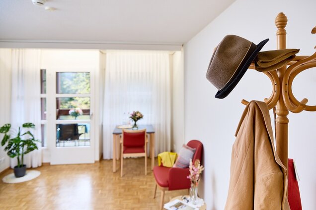 Detailansicht des Zimmers, Gardarobenständer, Pflanze, Tisch und Stuhl